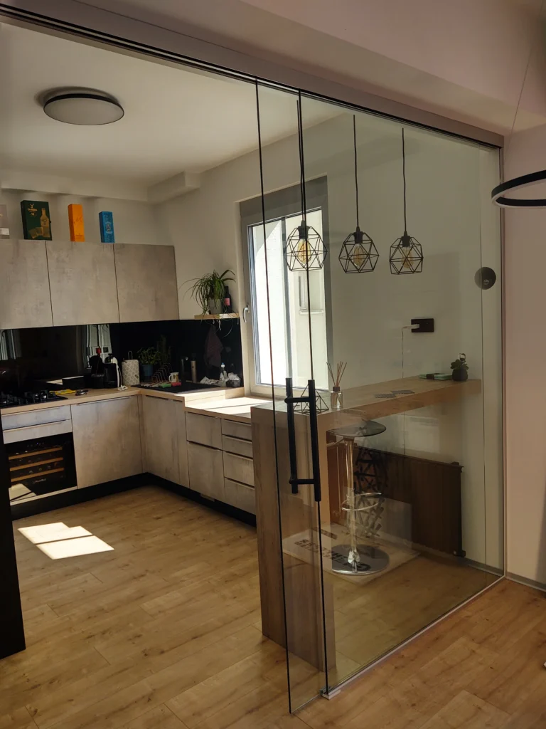 Bezrámová posuvná sklenená stena oddeľujúca kuchyňu od obývacej izby v modernom byte.