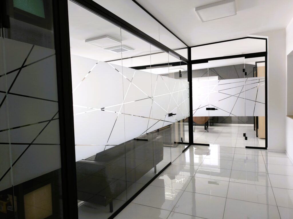 Bezrámové sklenené dvere so samozatváracími pántmi v modernej kancelárskej sklenenej stene.