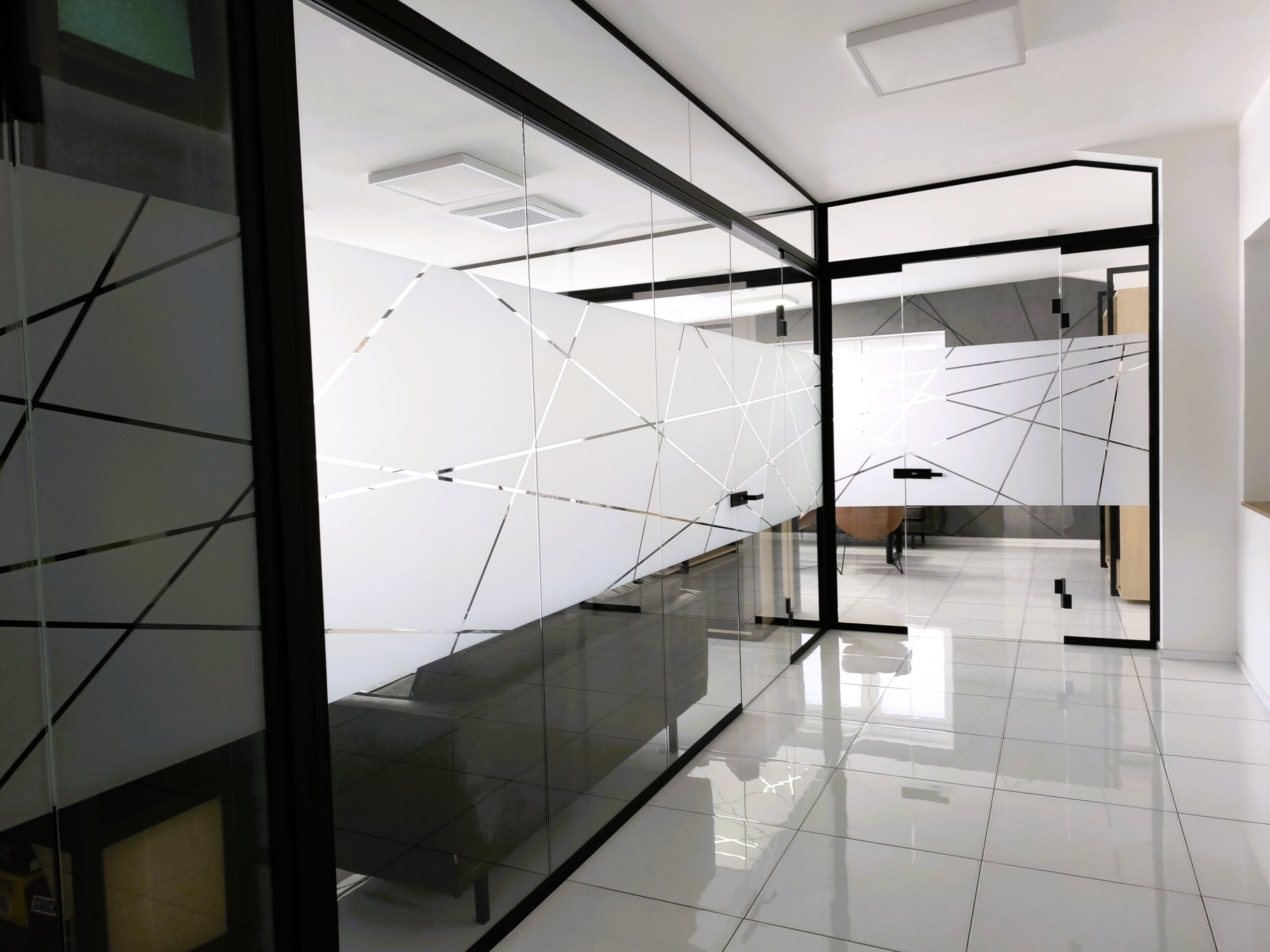 Bezrámové sklenené dvere so samozatváracími pántmi v modernej kancelárskej sklenenej stene.